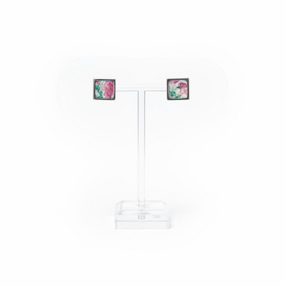 A pair of square stud earrings with colorful floral inlay and gold-toned and silver-toned borders, displayed on a clear acrylic T-stand with a white background.
