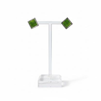 A pair of square stud earrings with green inlay and dark metal borders, displayed on a clear acrylic T-stand on a white background
