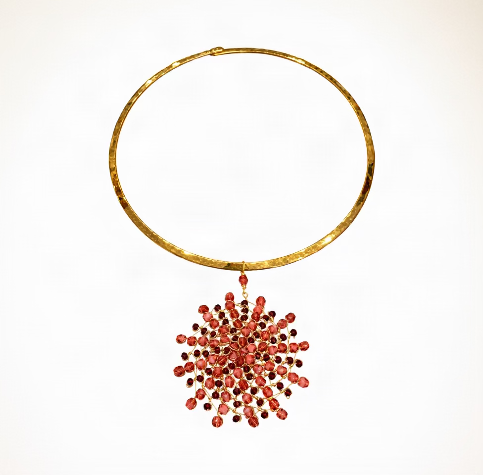 Un collier rigide rond doré avec une grappe pendante de perles rouges facettées, sur fond blanc.