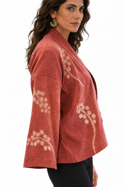 A dark haired woman dressed in black wearing a pink wool kimono jacket with a  white grey vine motif.