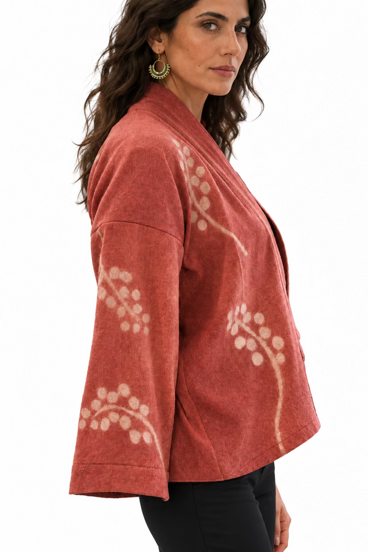 A dark haired woman dressed in black wearing a pink wool kimono jacket with a  white grey vine motif.