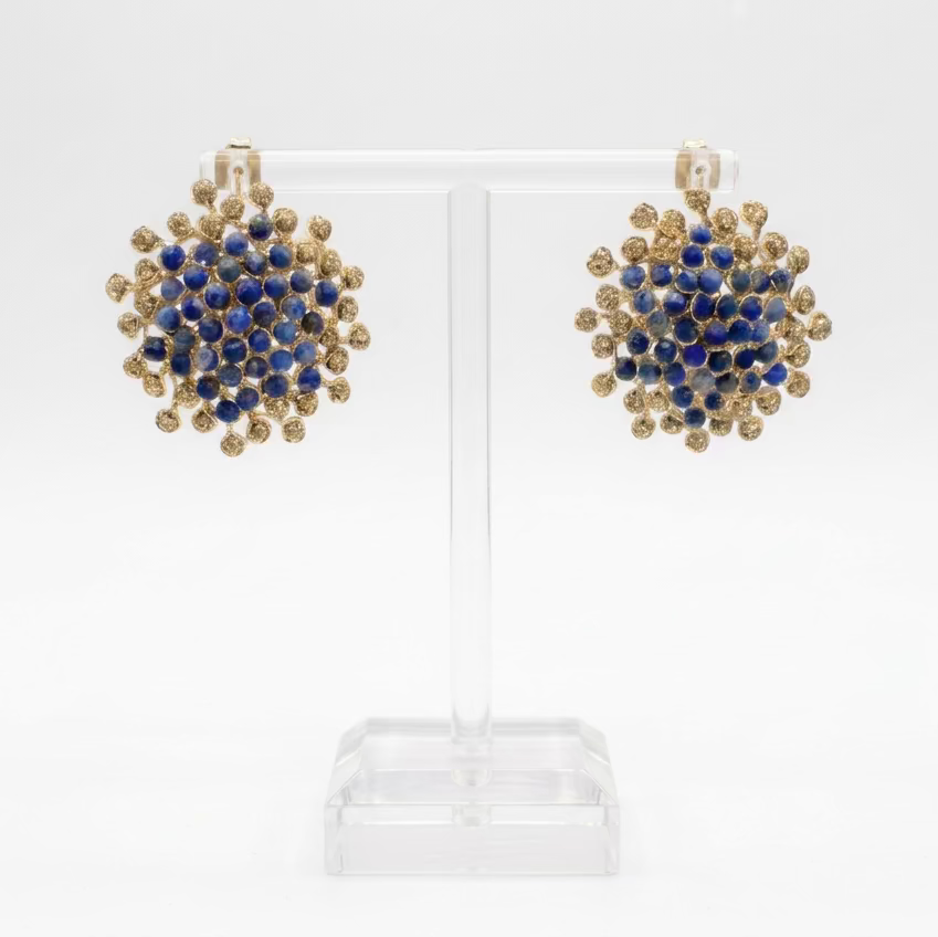 A pair of button earrings made from lapis lazuli and hematite stones on a gold plated wire, displayed on a clear acrylic stand.