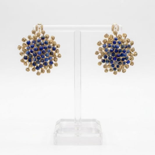 A pair of button earrings made from lapis lazuli and hematite stones on a gold plated wire, displayed on a clear acrylic stand.