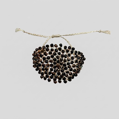 A wide cuff bracelet covered in faceted black bohemian crystals set in gold-toned metal, worn on a person's wrist against a white background.