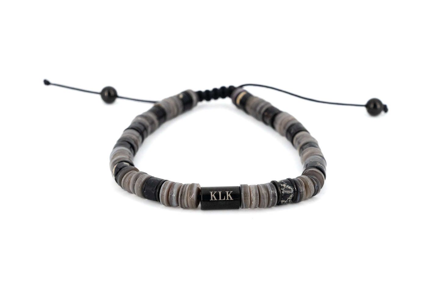 Men's bracelet with grey and black natural stone disc beads, black stainless steel KLK engraved centre bar and adjustable black cord fastening on white background
