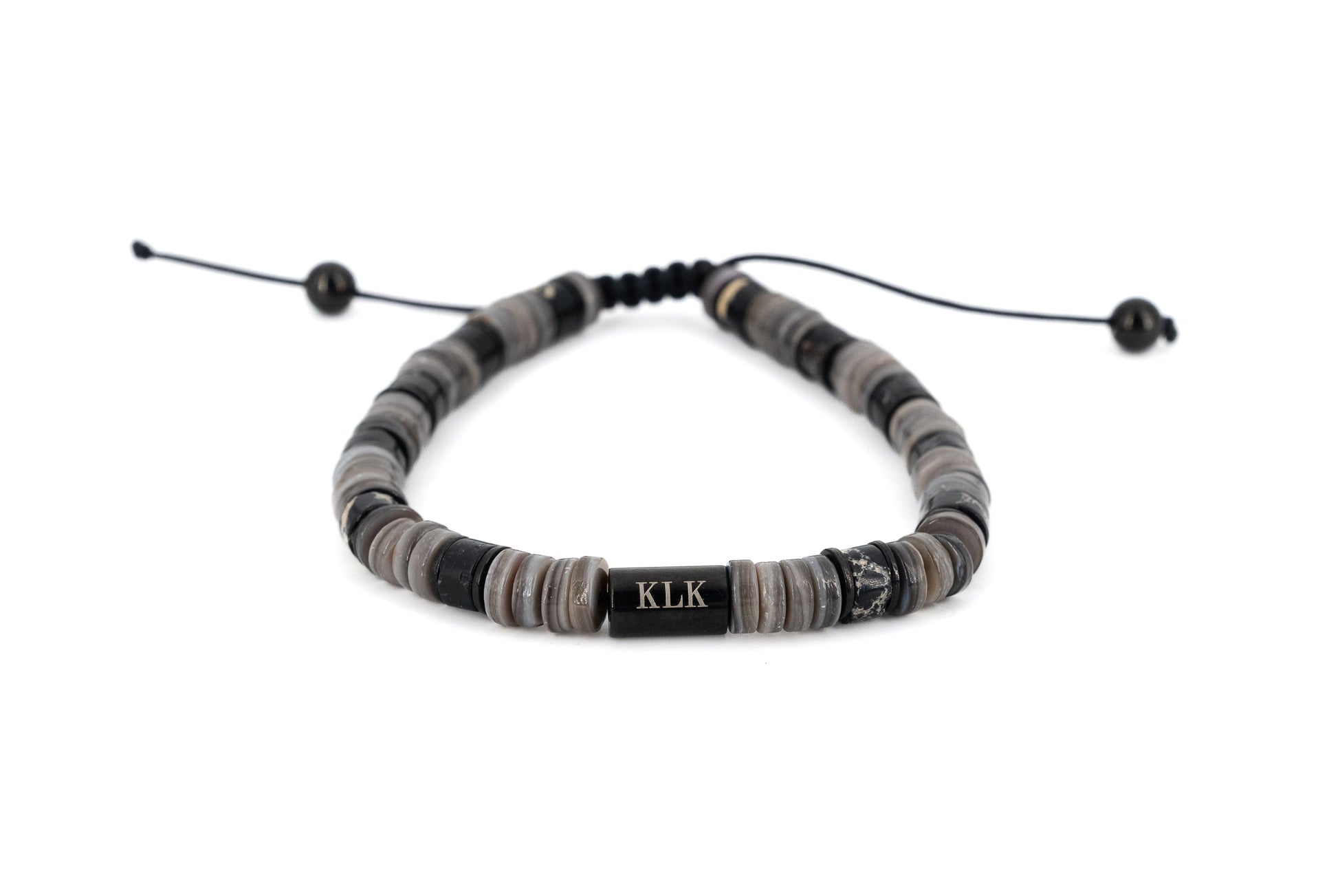 Men's bracelet with grey and black natural stone disc beads, black stainless steel KLK engraved centre bar and adjustable black cord fastening on white background