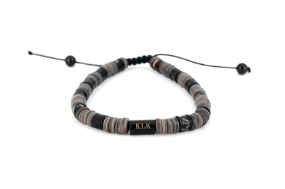 Men's bracelet with grey and black natural stone disc beads, black stainless steel KLK engraved centre bar and adjustable black cord fastening on white background