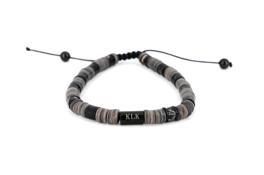 Men's bracelet with grey and black natural stone disc beads, black stainless steel KLK engraved centre bar and adjustable black cord fastening on white background