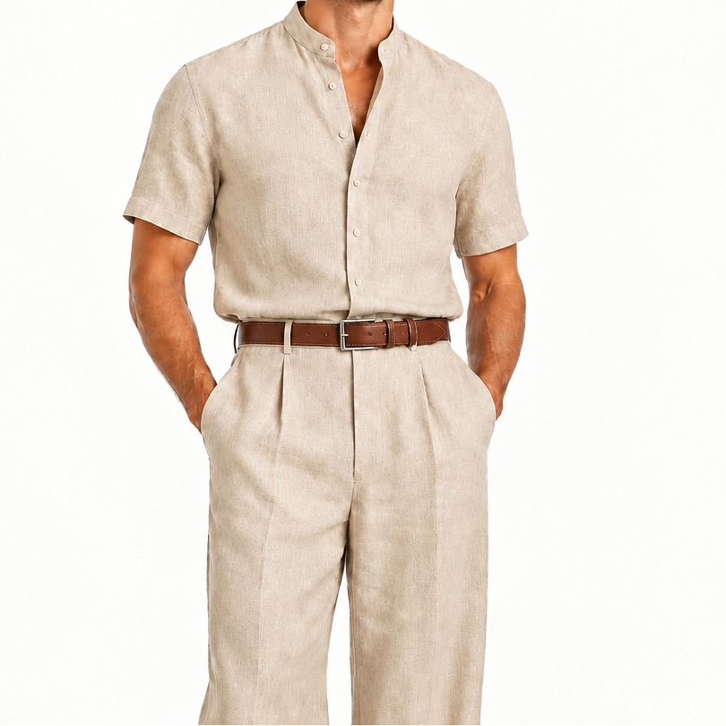 A man modeling a light beige linen short-sleeve button-up shirt and matching linen trousers, styled with a brown leather belt, against a plain white background.