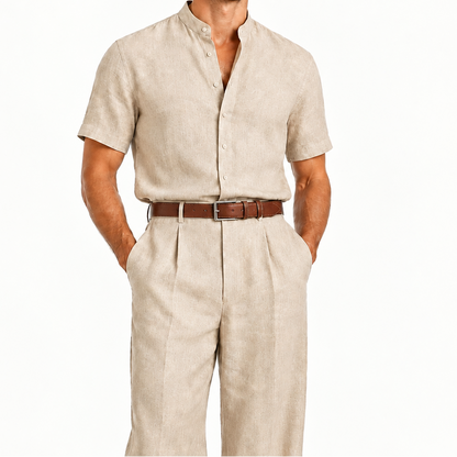 A man modeling a light beige linen short-sleeve button-up shirt and matching linen trousers, styled with a brown leather belt, against a plain white background.