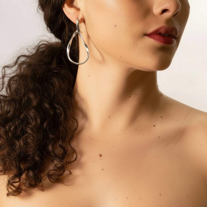 Close-up of a lady wearing silver organic hoop earrings with a neutral background