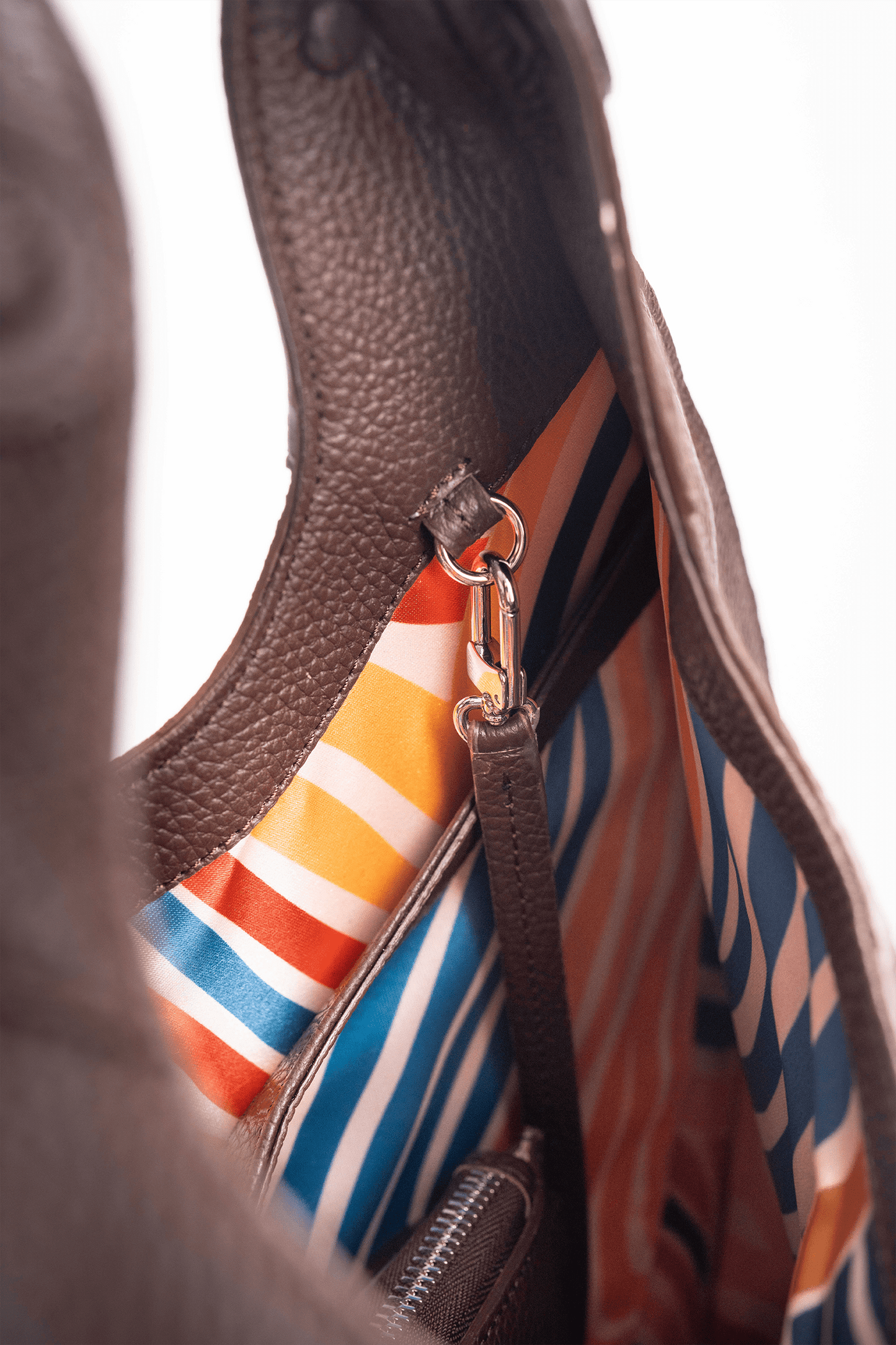 Inside view of the colourful lining of a brown pebble calf tote bag on a white background.