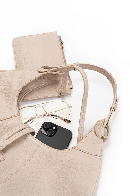 Beige handbag with a phone and glasses on a white background