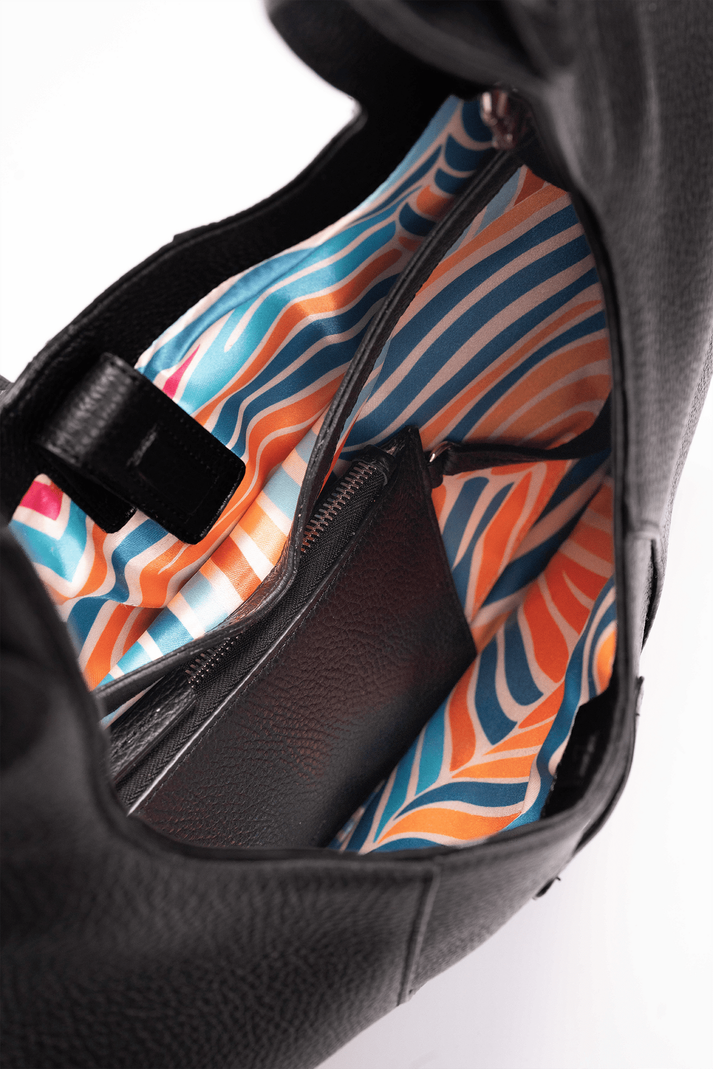 Inside view of the colourful lining of a black pebble calf tote bag on a white background.