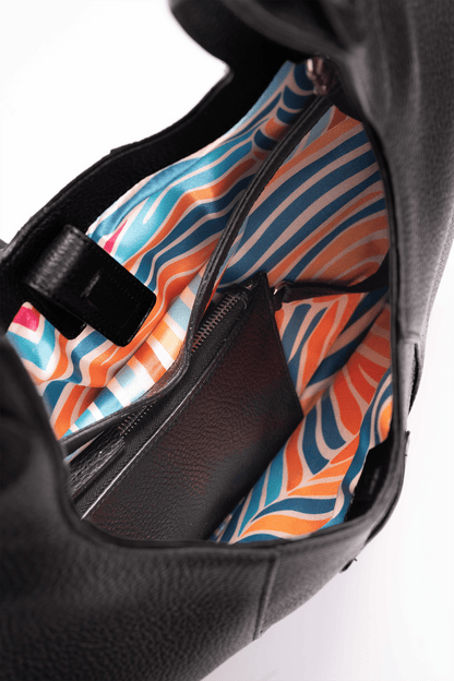 Inside view of the colourful lining of a black pebble calf tote bag on a white background.