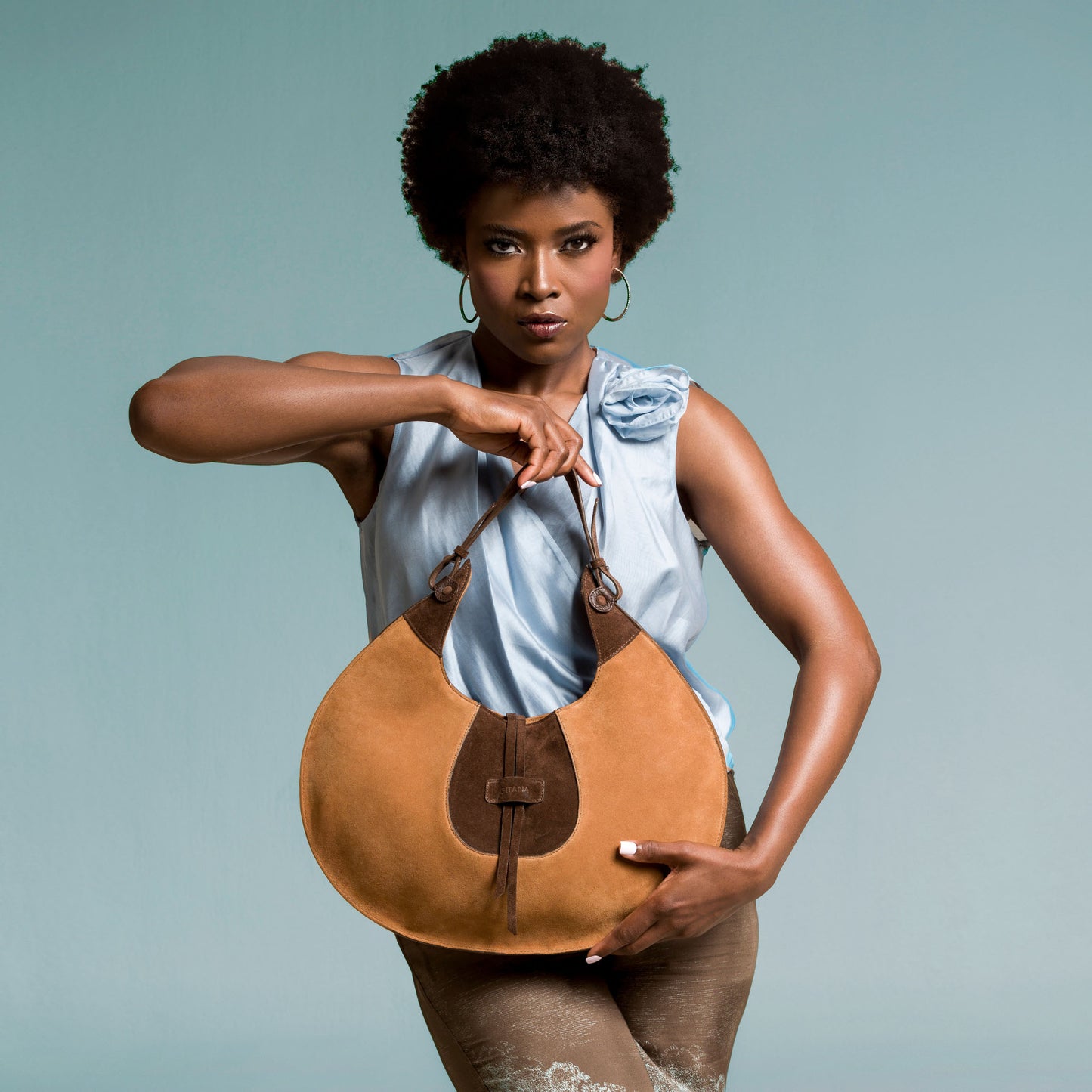 Woman holding a brown leather handbag against a gray background