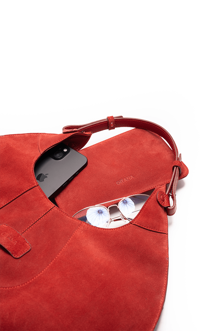 Red handbag with sunglasses and a phone on a white background