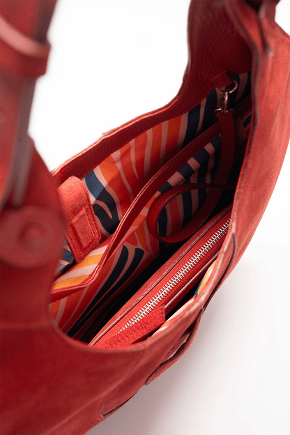 Inside view of the colourful lining of a scarlet suede tote bag on a white background.