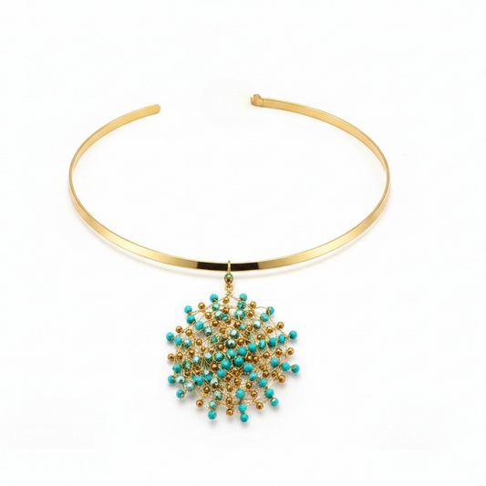 Gold-toned metal bangle necklace with a dangling starburst charm featuring turquoise blue beads and gold-toned metal details, shown on a plain white background.