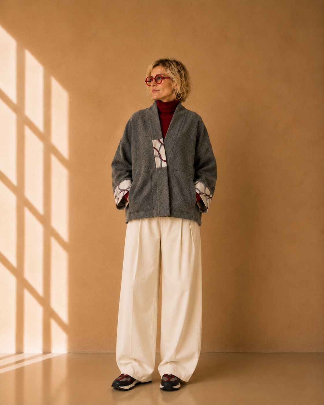Nuno Milano Aki grey felted Merino wool jacket, front view, with contrasting cream and burgundy abstract-print patch pocket and turned-back cuffs, open shawl collar, styled with cream wide-leg trousers and red turtleneck