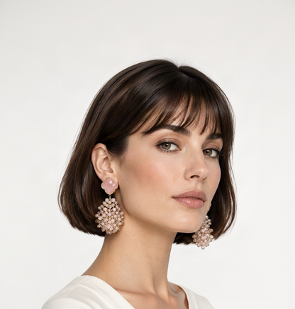 Une paire de boucles d'oreilles pendantes statement dorées avec puces trèfle rose pâle et grappes de pierres transparentes et blanches en cascade, portées par une mannequin au carré court.