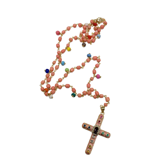 A rosary necklace featuring coral-pink faceted beads, gold-tone chain links, and a gold-tone cross pendant embellished with small multicolored gemstones, shown on a plain white background.