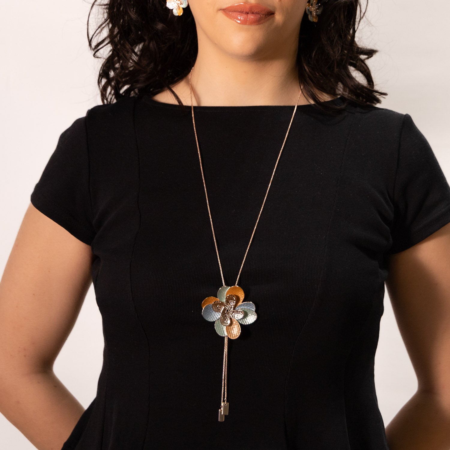 Model wearing the Double Flower Zamak Necklace in rose gold with turquoise and amber hand-painted enamel over a black dress. 