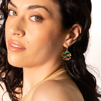 Close-up of a woman wearing a gold earring with a green & gold enamel on a white background