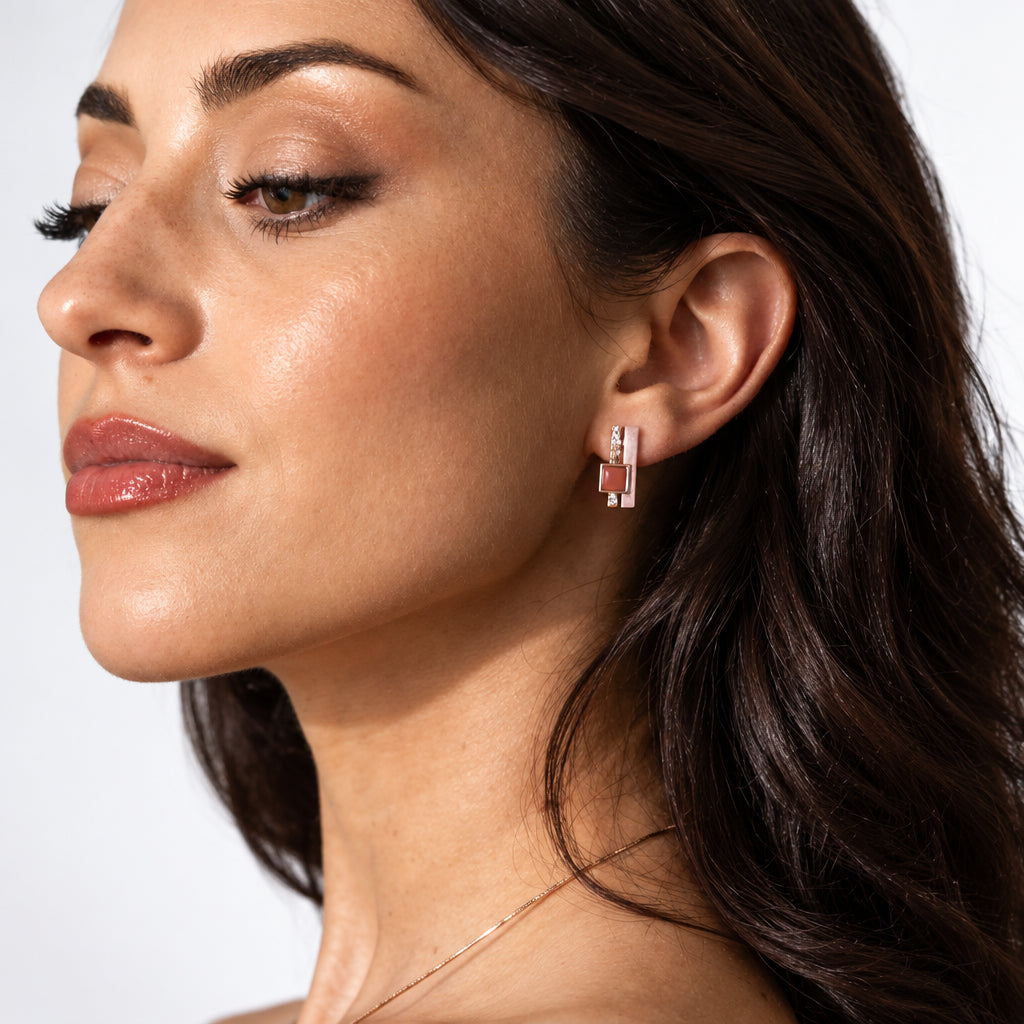 A close-up side profile of a woman with dark hair wearing a pair of slim bars, one hand-painted in soft lilac, one hammered rose gold, sit side by side, punctuated by a warm burgundy resin square for a little graphic contrast, against a clean white background.
