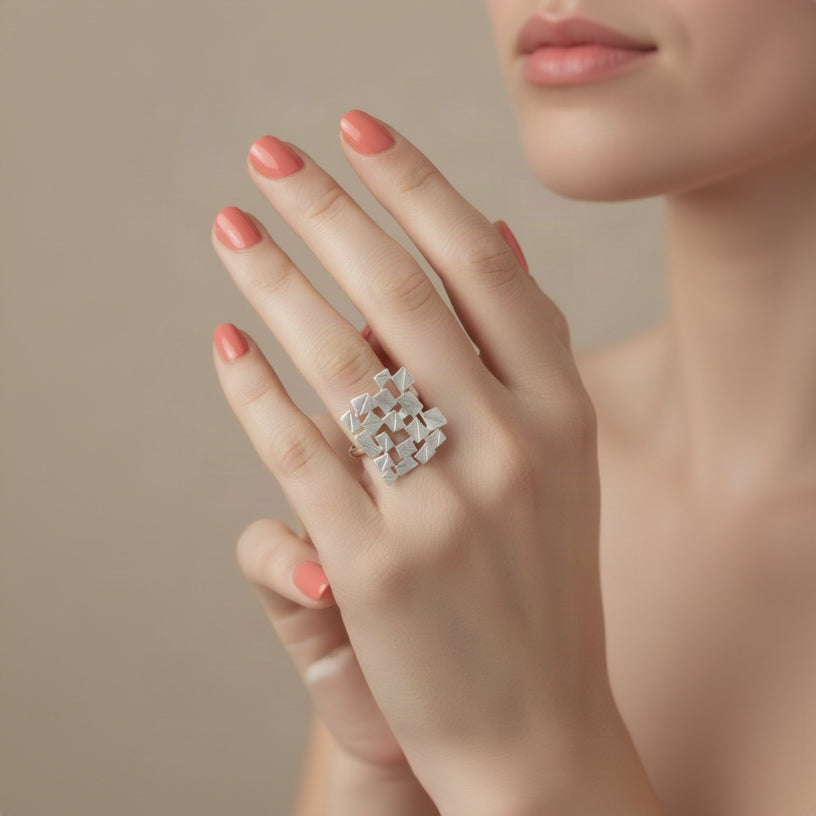 A silver textured geometric ring with a faceted, angular design, worn on a manicured hand.