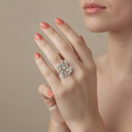 A silver textured geometric ring with a faceted, angular design, worn on a manicured hand.