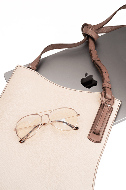 Beige calf leather crossbody handbag displayed with MacBook and glasses on a white table to show bag capacity and lifestyle use.