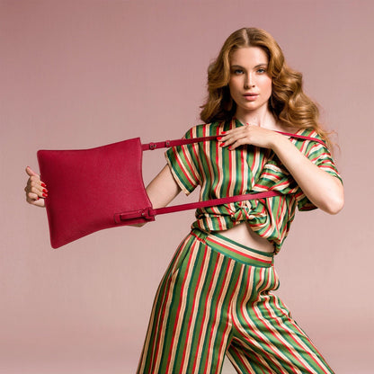 Woman in a striped outfit holding a red handbag against a pink background