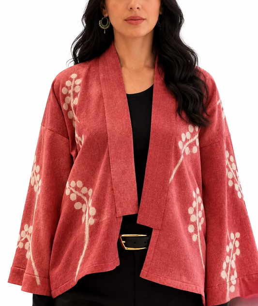 A dark haired woman dressed in black wearing a pink merino wool kimono lightweight jacket with a vine design 