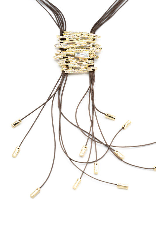 Long Abstract Necklace with Crystal in gold, showing the textured rectangular Zamak pendant with crystal detail and cascading dark waxed cords with gold-tipped ends, product shot on white background