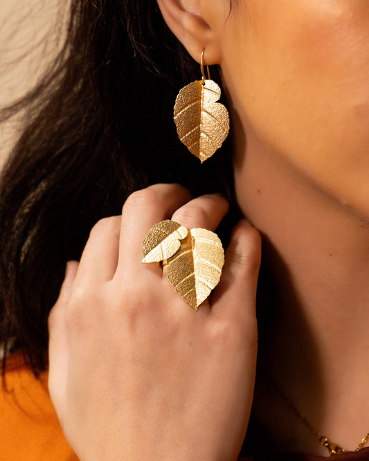 Close-up of model wearing Matt Gold Brass Birch Leaf Earrings with a matching leaf ring, styled over an orange top with warm-toned lighting