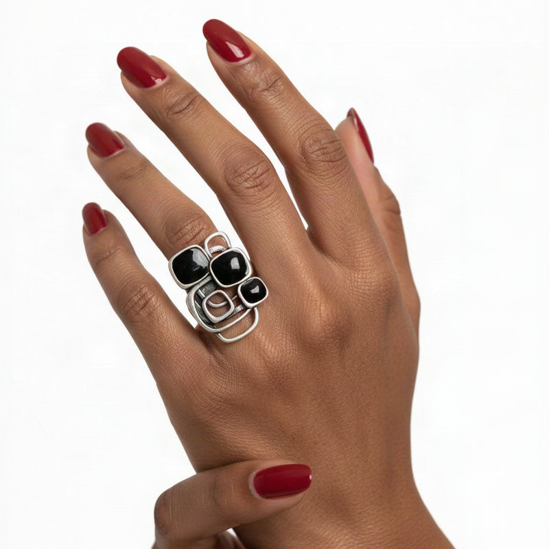 A mosaic black resin and silver ring on a beautiful manicured hand against a white background.