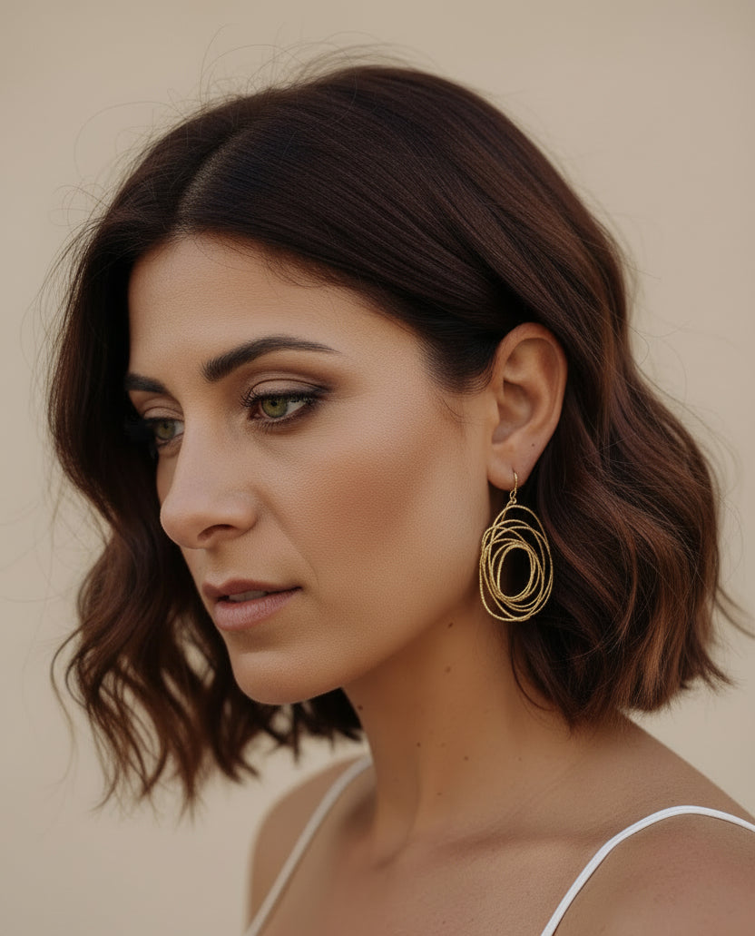A woman with a wavy bob wearing large gold-toned geometric hoop earrings and a white top