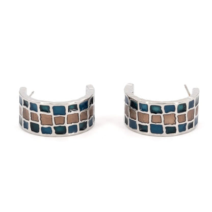 A pair of silver-toned huggie hoop earrings featuring a mosaic pattern of blue and brown square tiles, shown on a plain white background.
