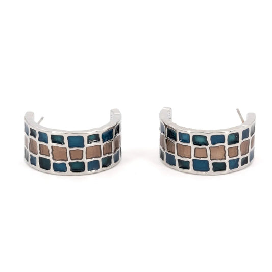 A pair of silver-toned huggie hoop earrings featuring a mosaic pattern of blue and brown square tiles, shown on a plain white background.