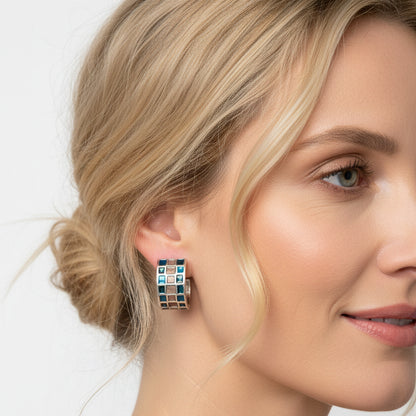 A blonde girl wearing a pair of huggie hoop stud earrings against a white background.